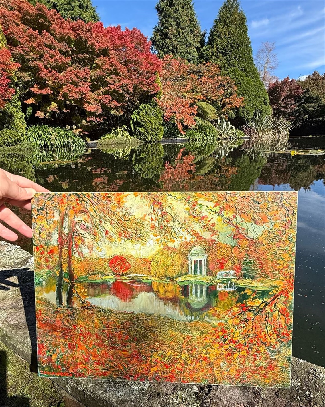 Painting of a landscape being held up against a photo of the same landscape